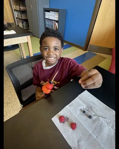 Smiling young student at a classroom table with a small snack