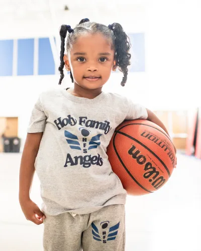 Young student in a Holy Family Angels shirt holding a basketball in the gym