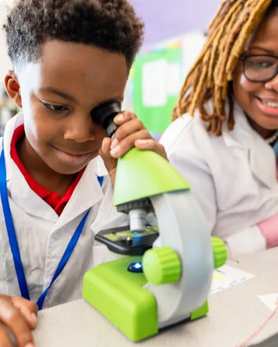 Students in lab coats working together at a microscope in the classroom